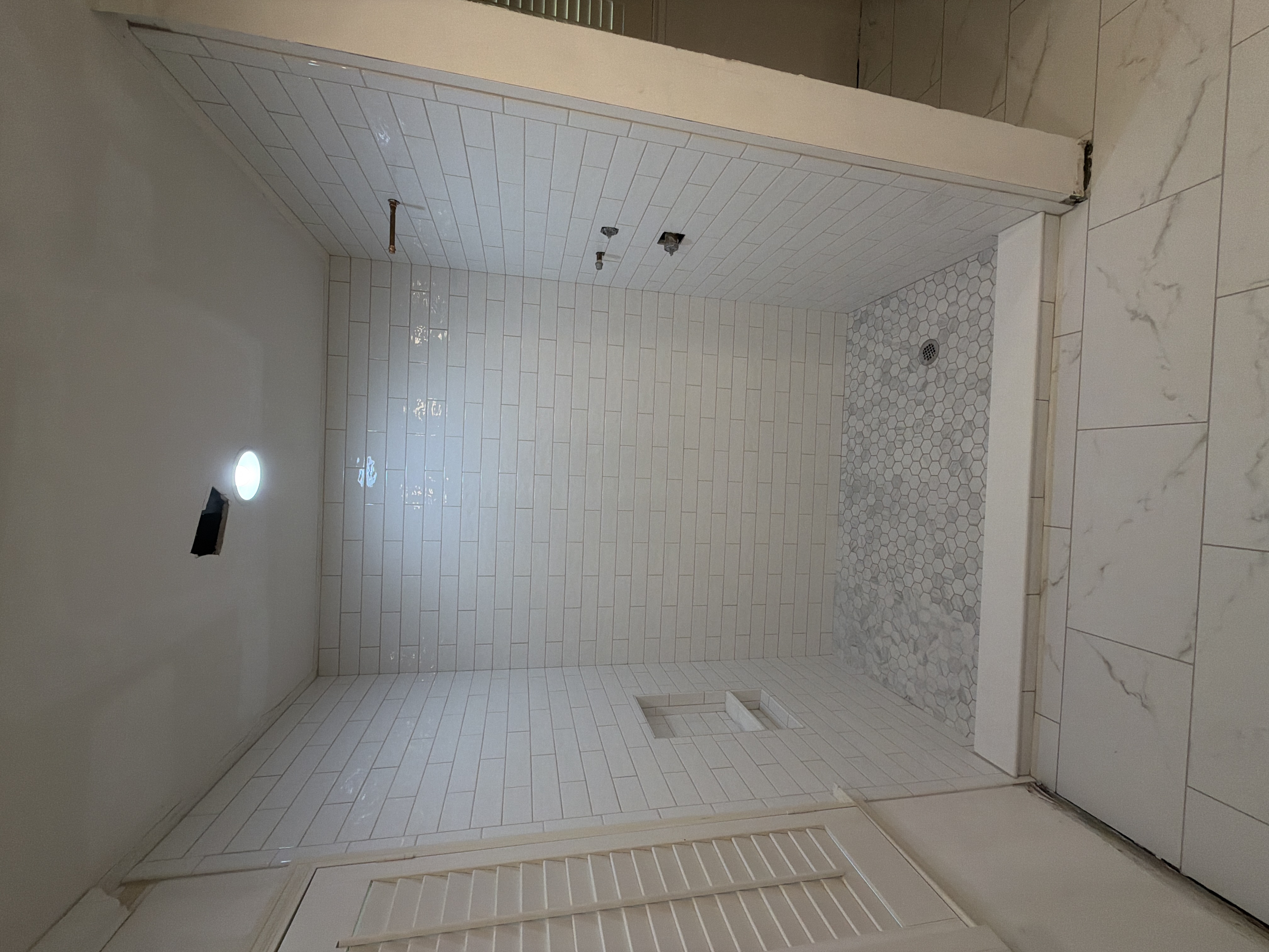 White subway tile shower with marble mosaic flooring
